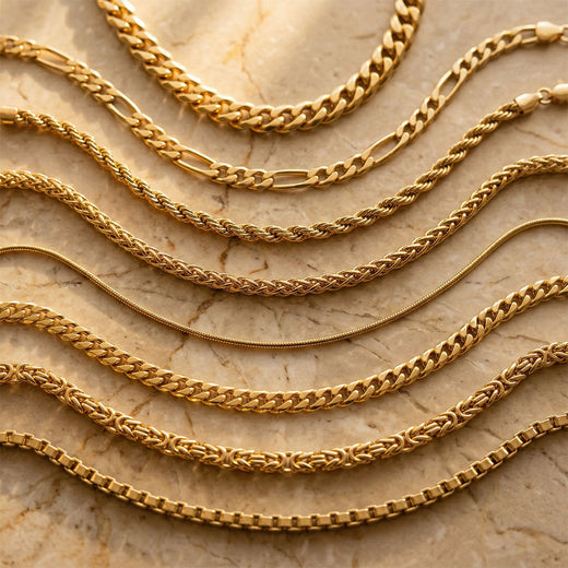 Seven gold-plated chains in different weaves arranged in waves on pale marble