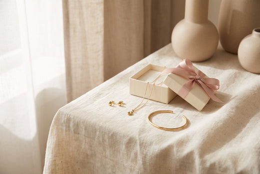 Gold-plated earrings, fine necklace and bracelet beside a gift box with pink ribbon