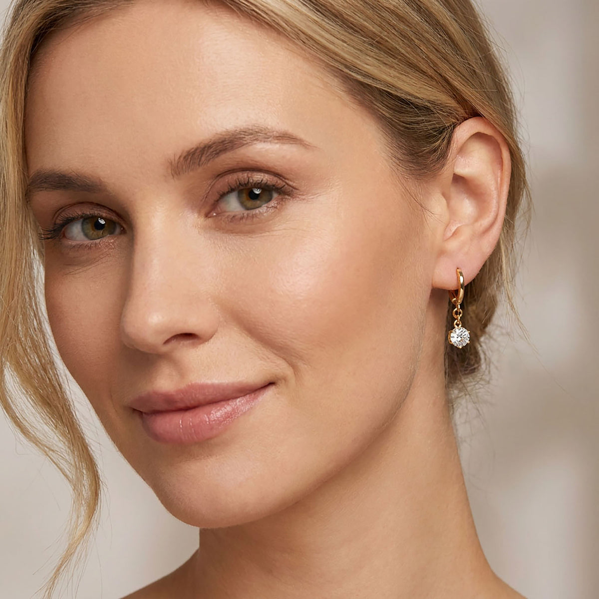 Gold-plated drop earring with a round clear cubic zirconia and French hook on a model's ear