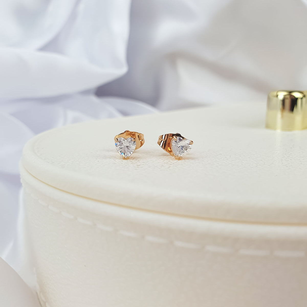 Gold-plated studs with heart-cut clear cubic zirconia on a cream jewellery box