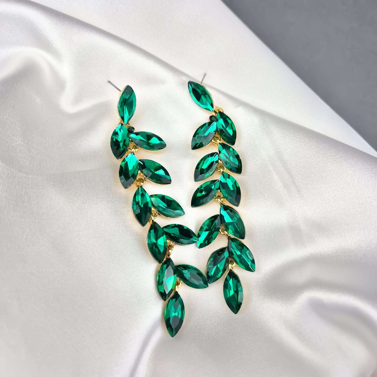 Green crystal leaf earrings on white satin with push-back posts visible