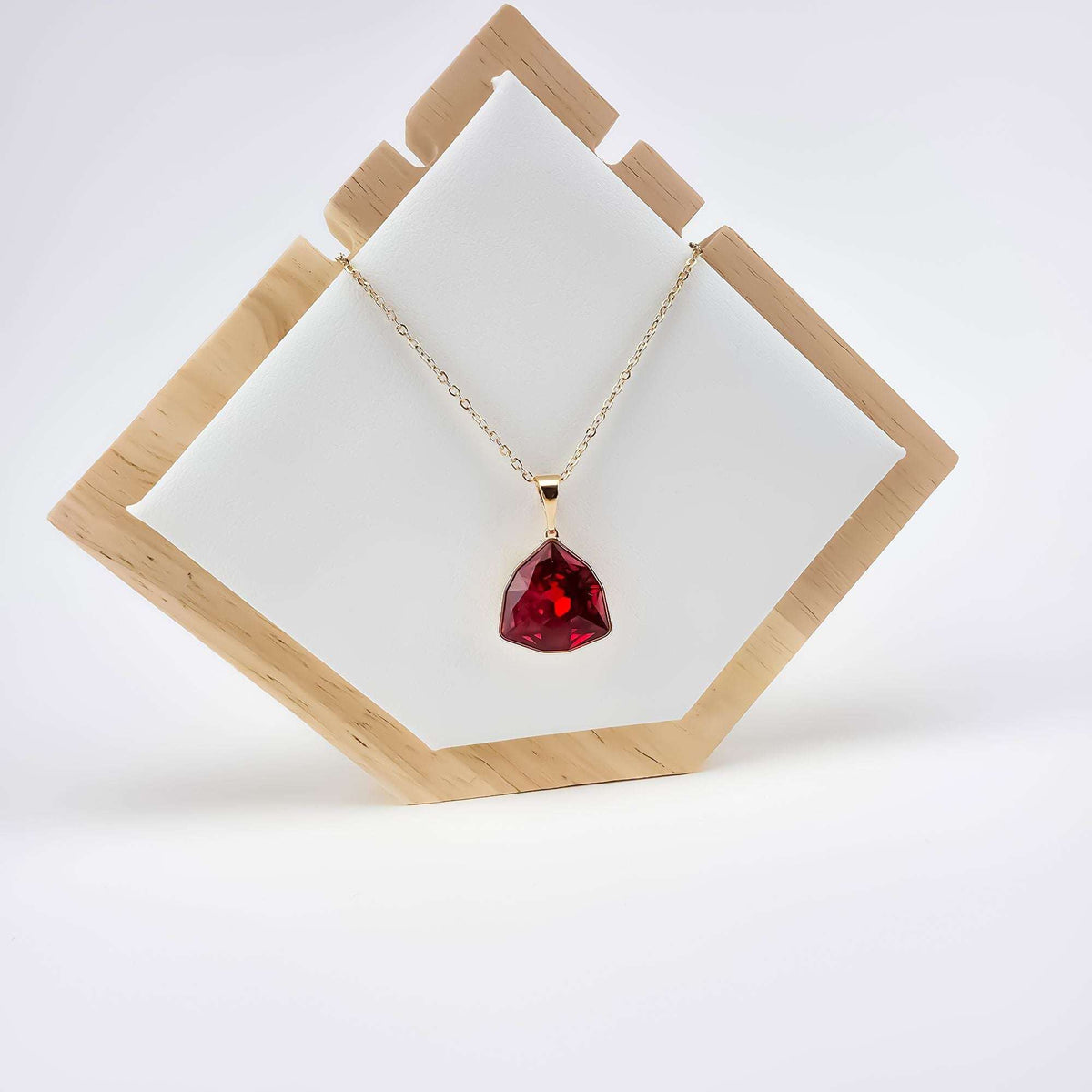 Gold-plated necklace with a red crystal pendant on a light wooden stand