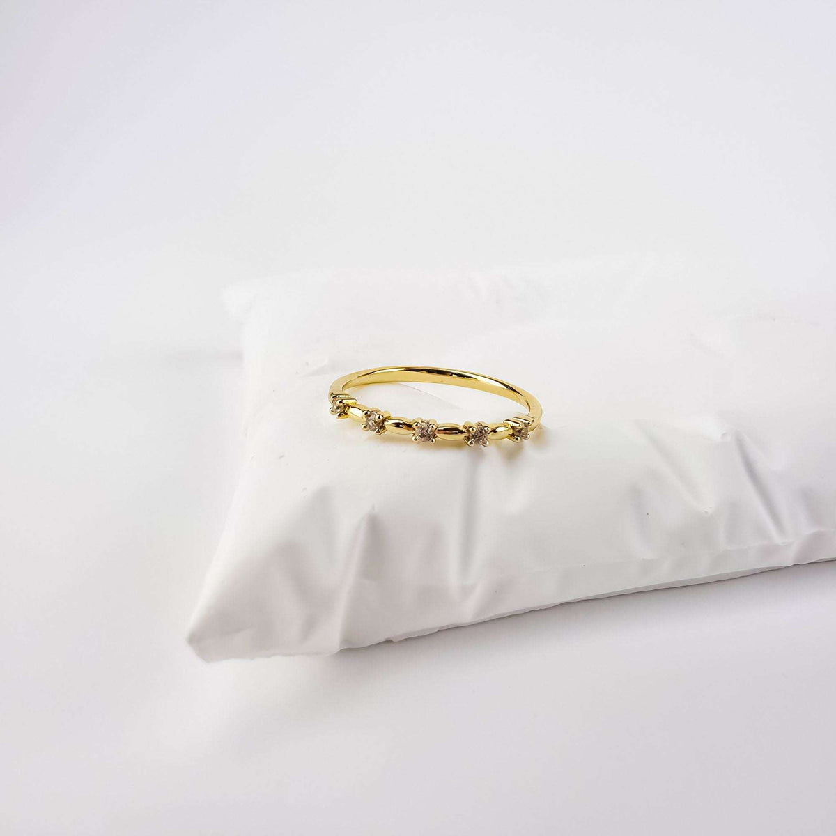 Gold-plated cubic zirconia ring on a white cushion, side view of the slim band