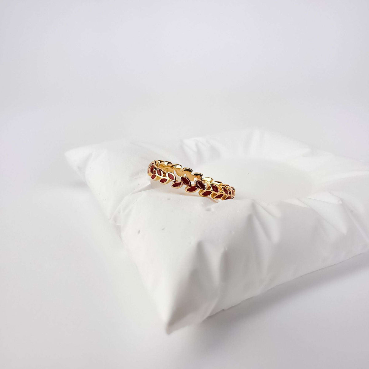 Gold-plated leaf ring with dark red enamel, side view on a white cushion