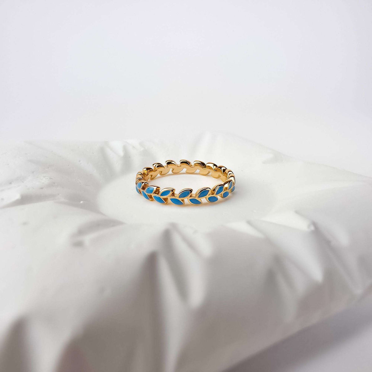 Gold-plated leaf wreath ring with blue enamel on a white ceramic cushion