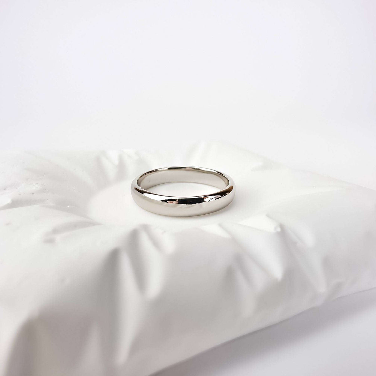 Classic smooth platinum-plated ring standing on a white ceramic cushion