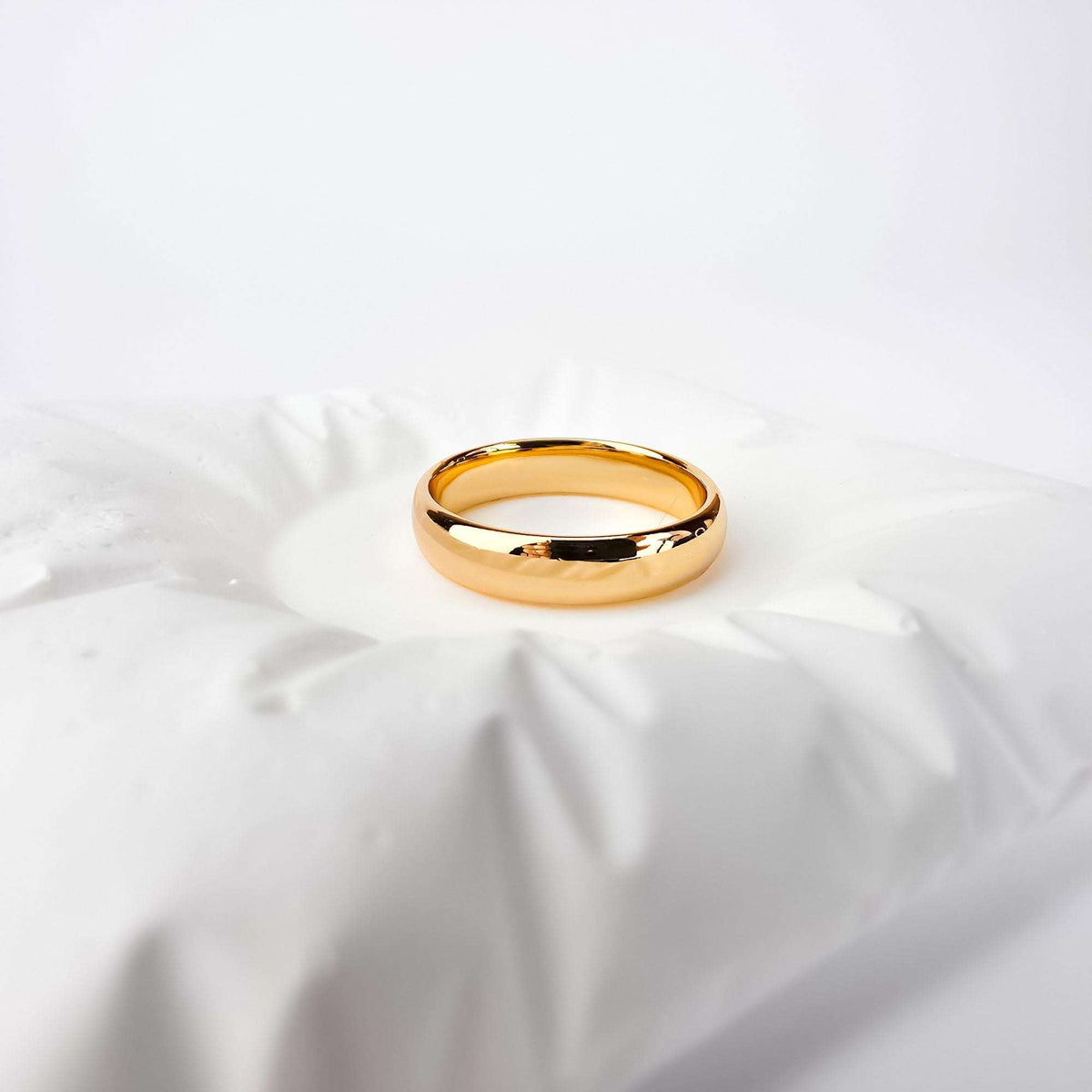 Gold-plated wedding band with a rounded profile and mirror shine on white fabric