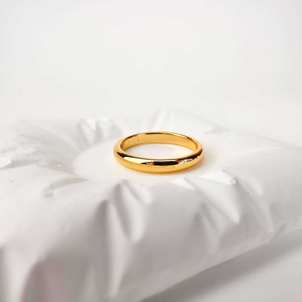 Gold-tone wedding band in side view on crumpled white fabric, domed profile
