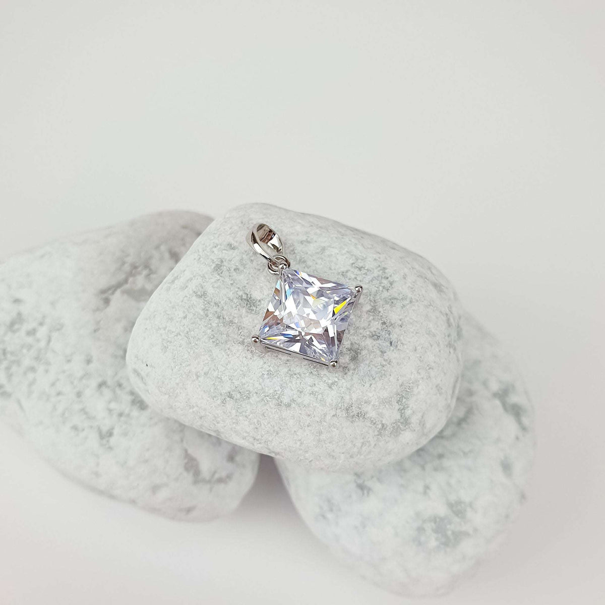 Silver | Silver-tone square stone pendant on light pebbles, side view of sparkling facets