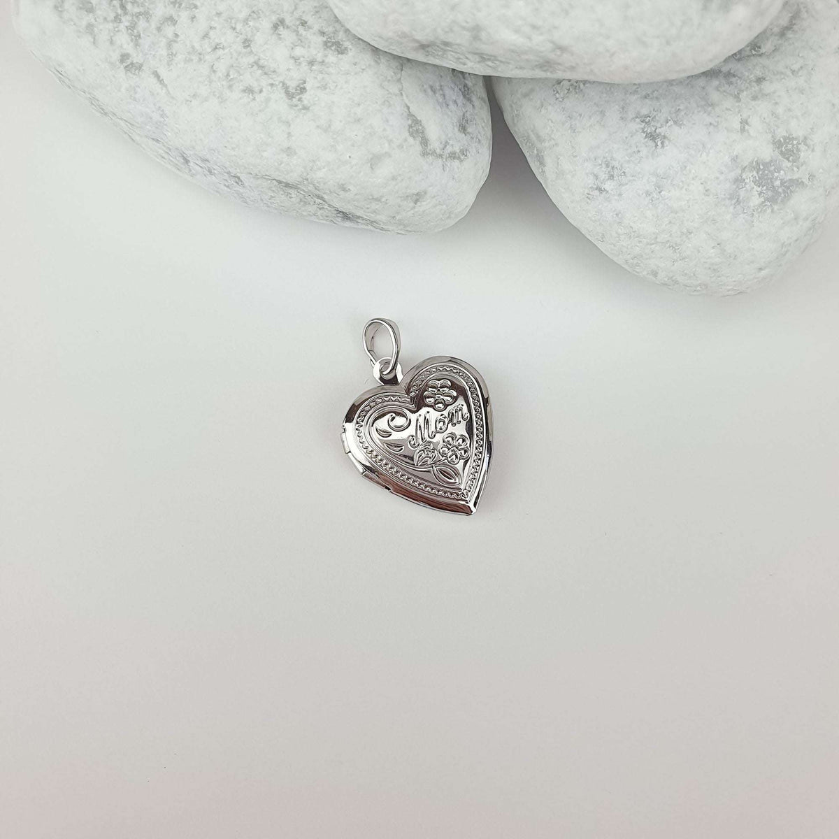 Polished heart locket with fine raised detail on a light surface beside stones