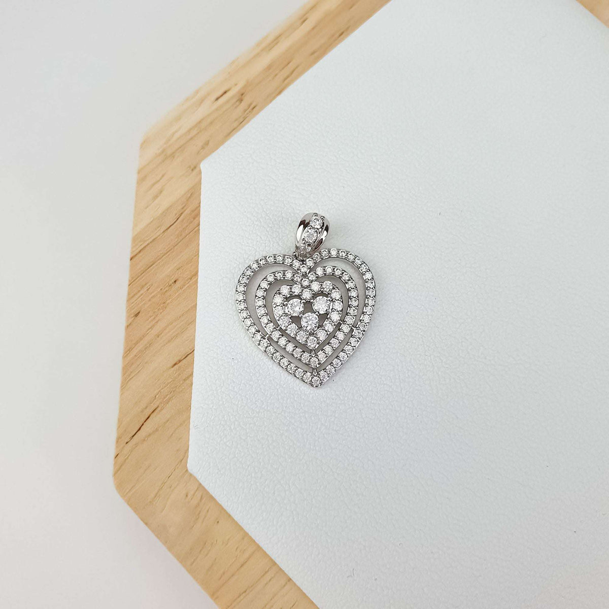 Sparkling silver-tone heart pendant on a light leather stand with a wooden edge