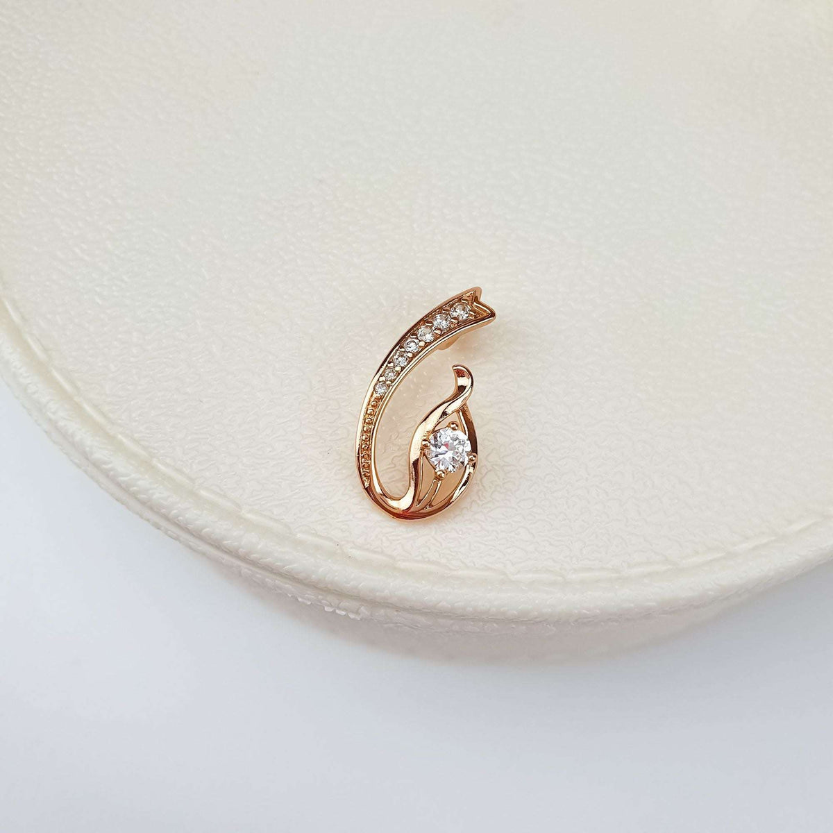 Gold-tone pendant with a warm pinkish hue and a central cubic zirconia, close up on a cream ceramic stand