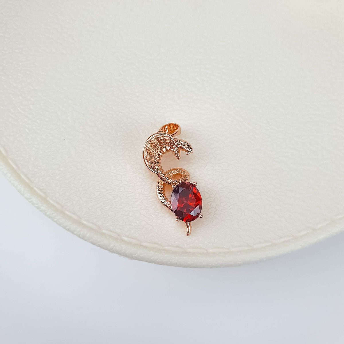 Close-up of snake pendant with a red oval cubic zirconia on cream ceramic
