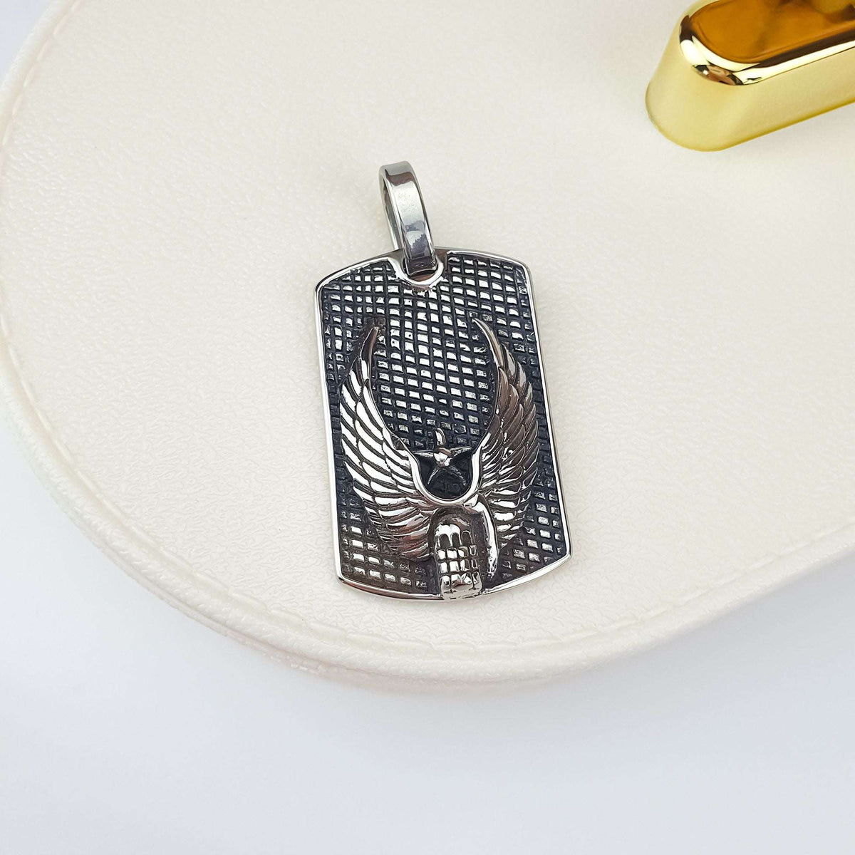 Silver-tone winged skull tag pendant, close up on cream ceramic