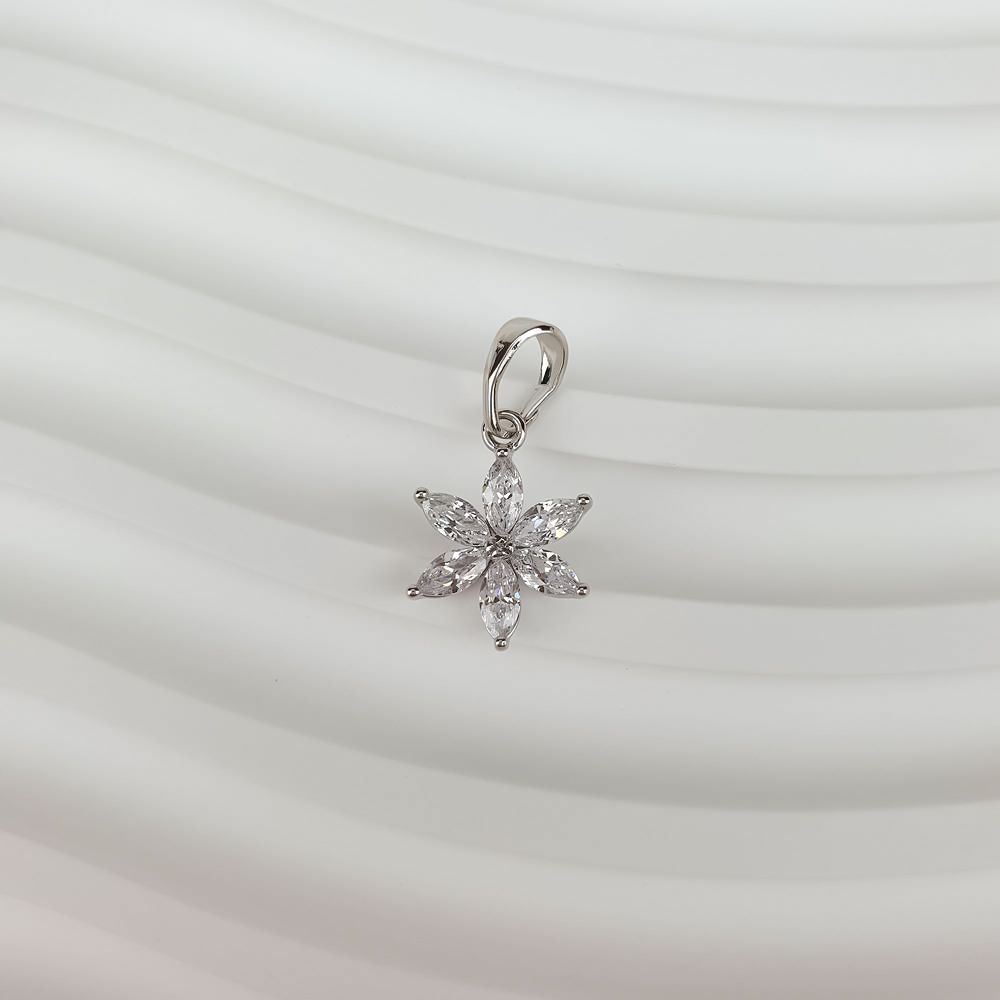 Sparkling silver-tone flower pendant on a wavy white surface, loop visible