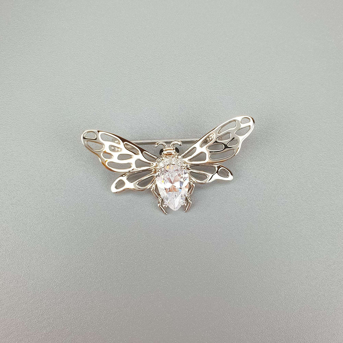 Bee brooch with openwork wings and a teardrop stone, top view on grey