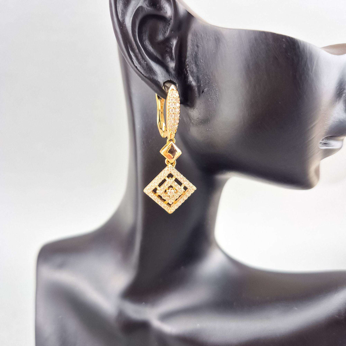 Gold-plated rhombus earrings with cubic zirconia shown on a dark mannequin ear