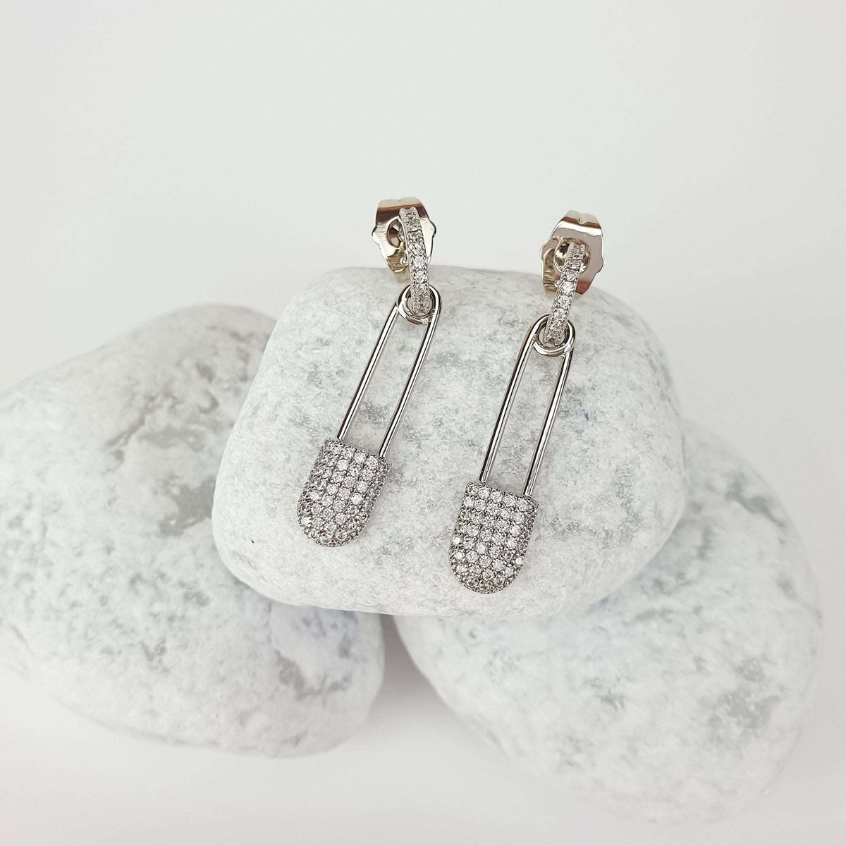 Silver-tone safety pin earrings set with cubic zirconia, at an angle on white stones