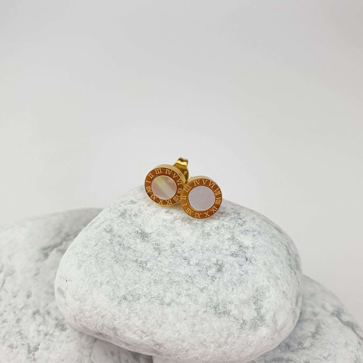 Gold-tone button studs with Roman numerals and faux pearl, side view on white stone