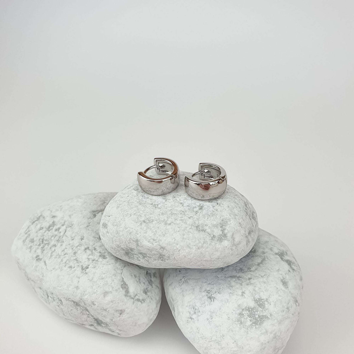 Small silver-tone hoop earrings on white pebbles, smooth clasp mechanism visible