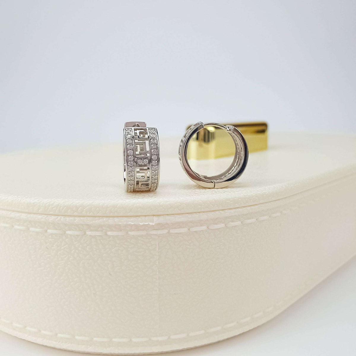 Pair of silver-tone earrings on a cream box showing the meander and clasp
