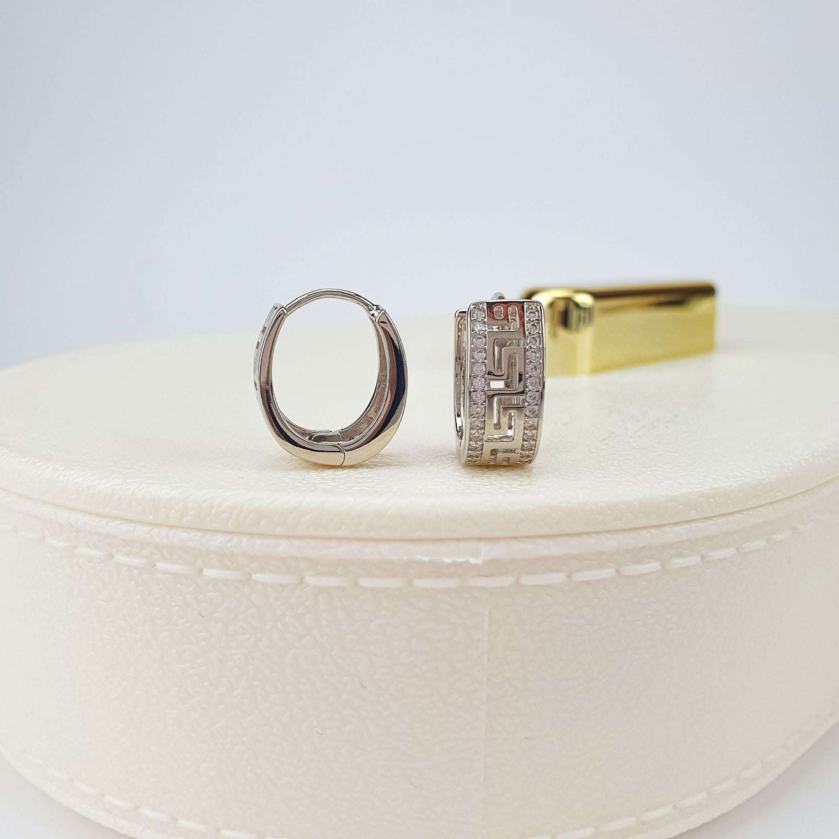 Platinum-tone Greek key earrings shown from the side and front on a cream box