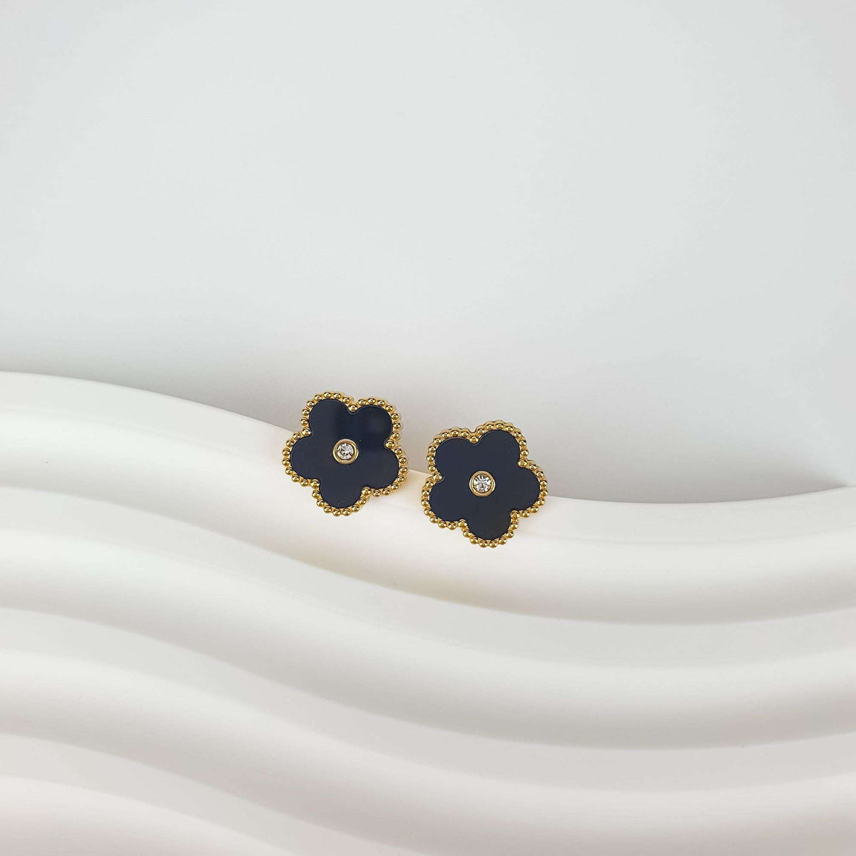 Pair of black enamel flower earrings with sparkling cubic zirconia centres on light fabric