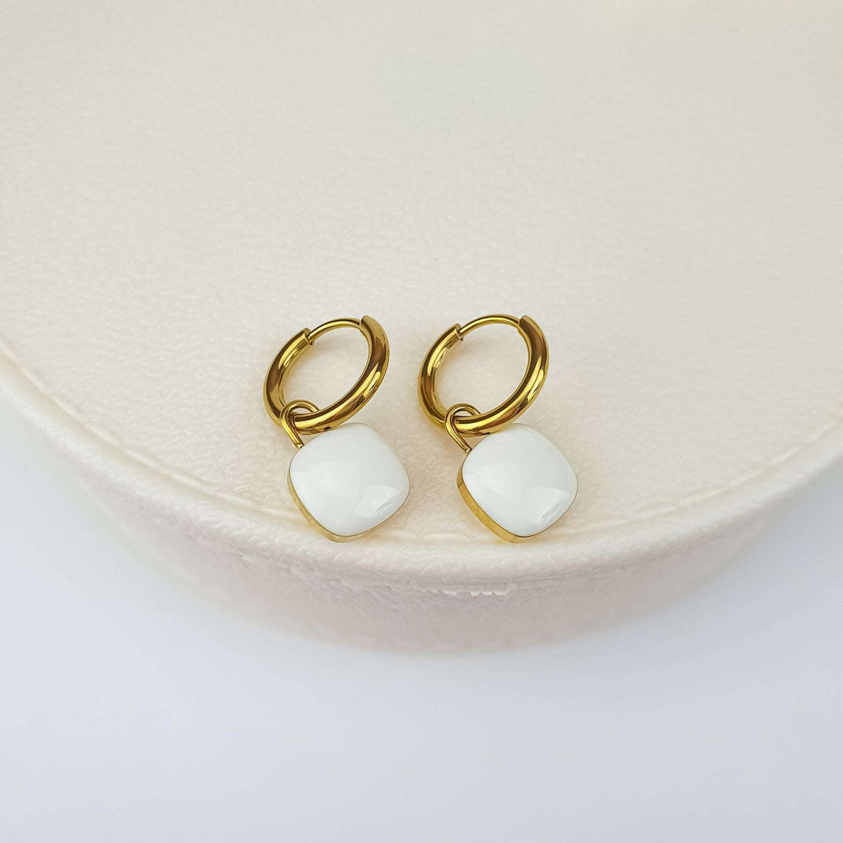 Gold-plated hoops with a removable white square enamel charm on a light box
