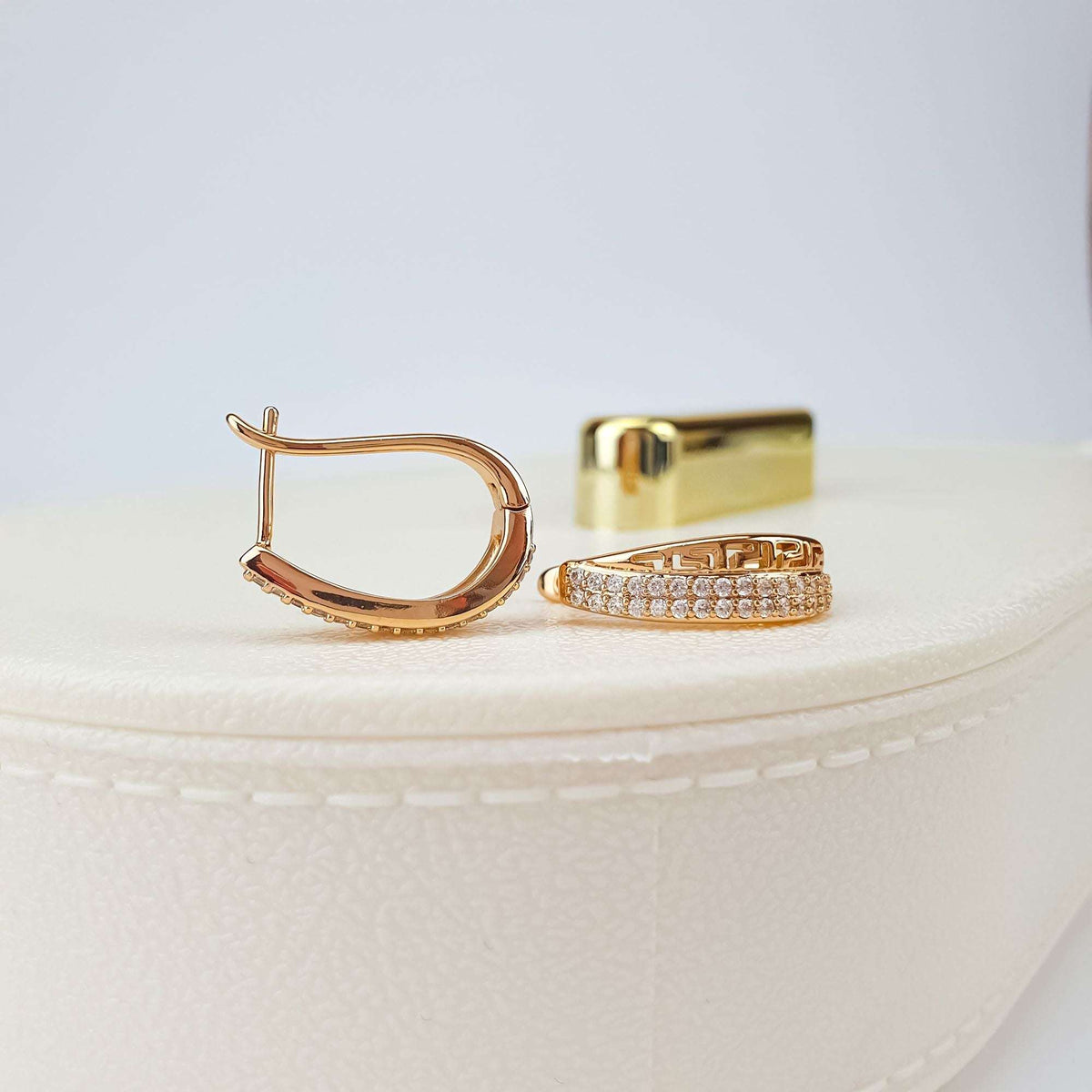 Pair of gold-plated earrings on a light box, leverback clasps and stone rows visible