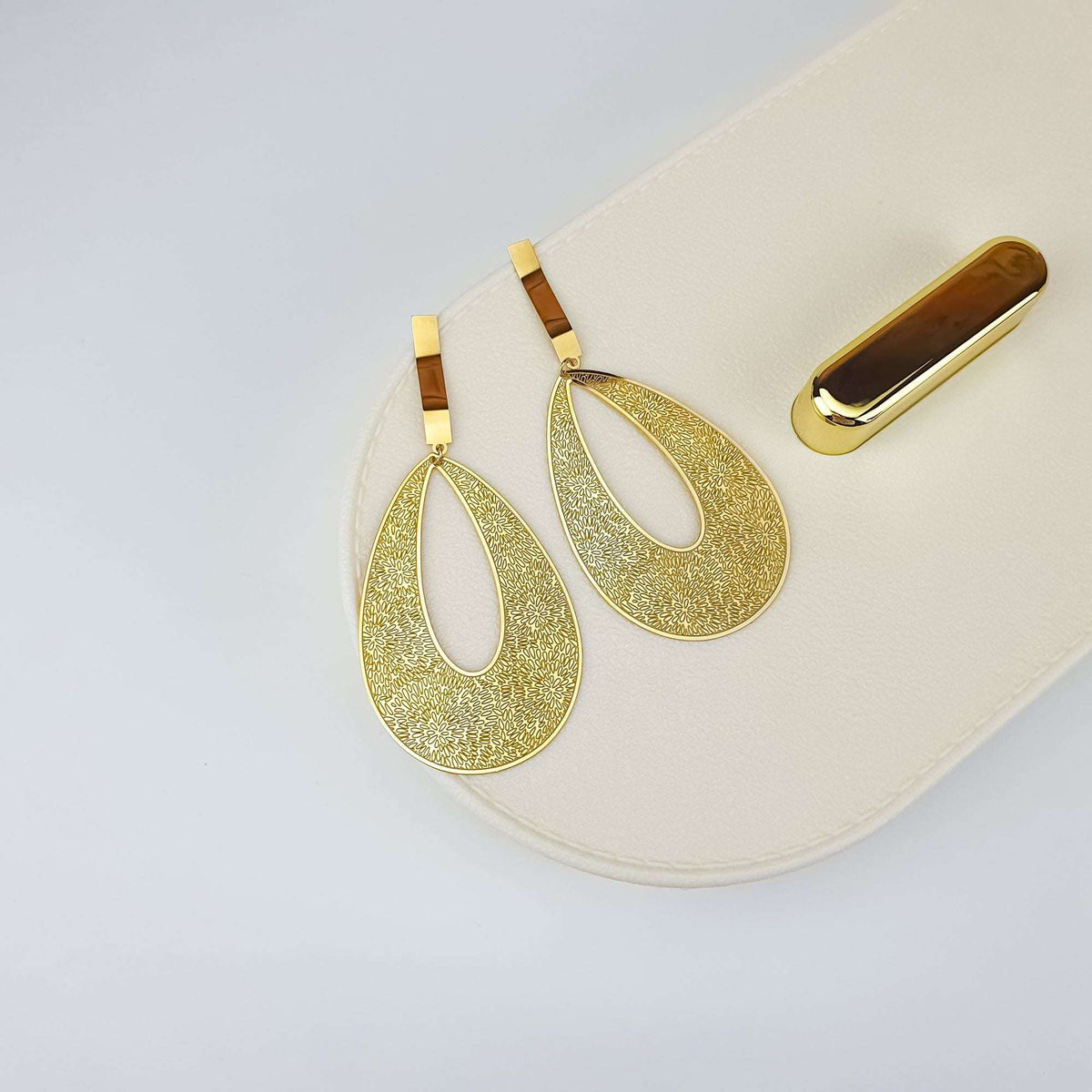 Gold-plated teardrop earrings with a floral pattern on a cream jewellery box