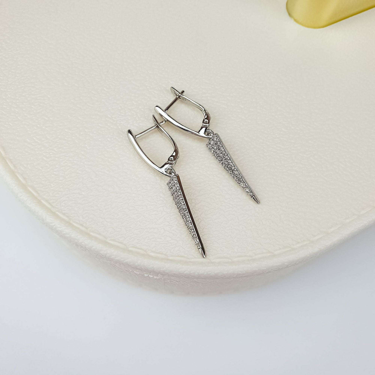 Pair of earrings with pointed, zirconia-paved drops on a cream background