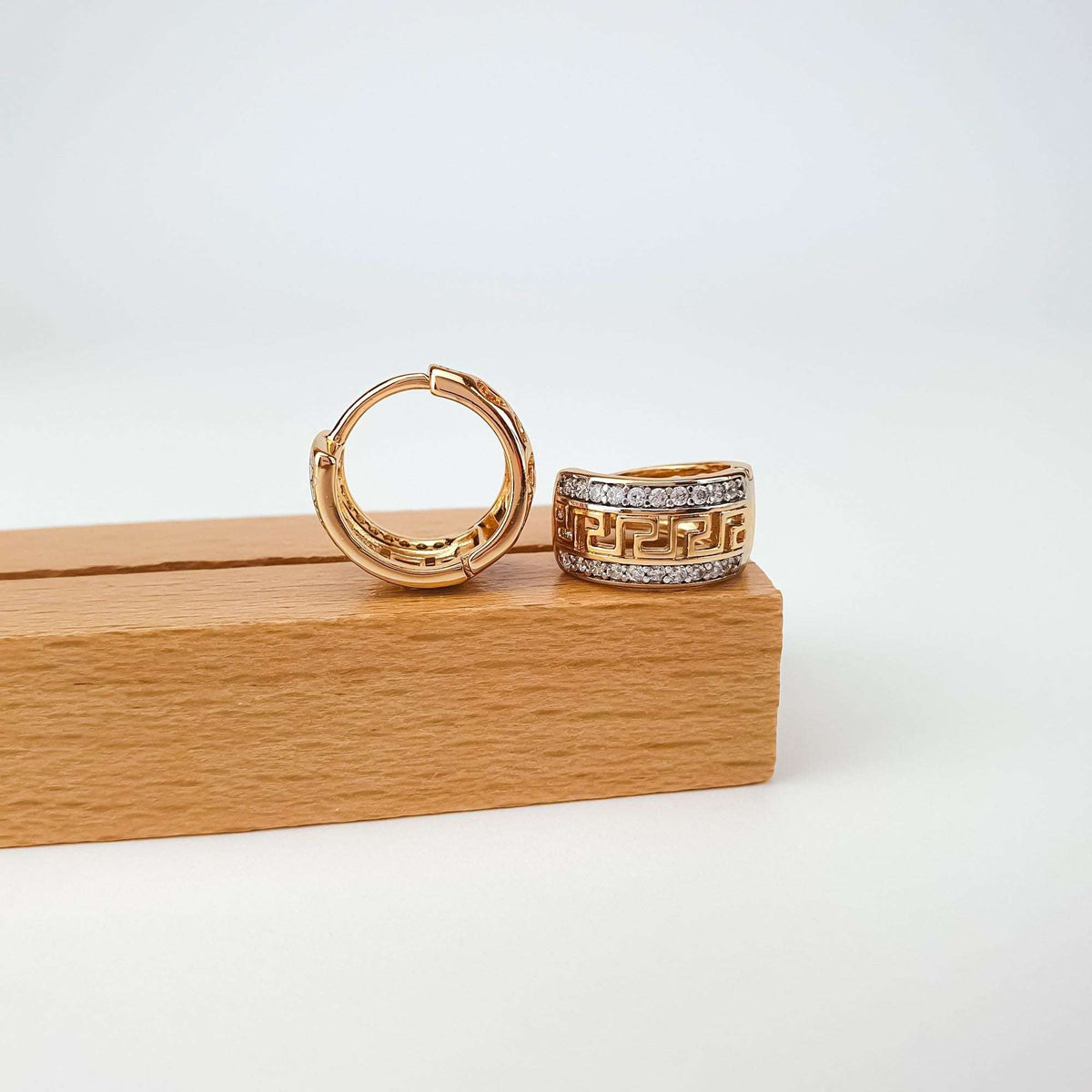 Pair of gold-tone hoop earrings on a wooden block, Greek pattern and clasp visible