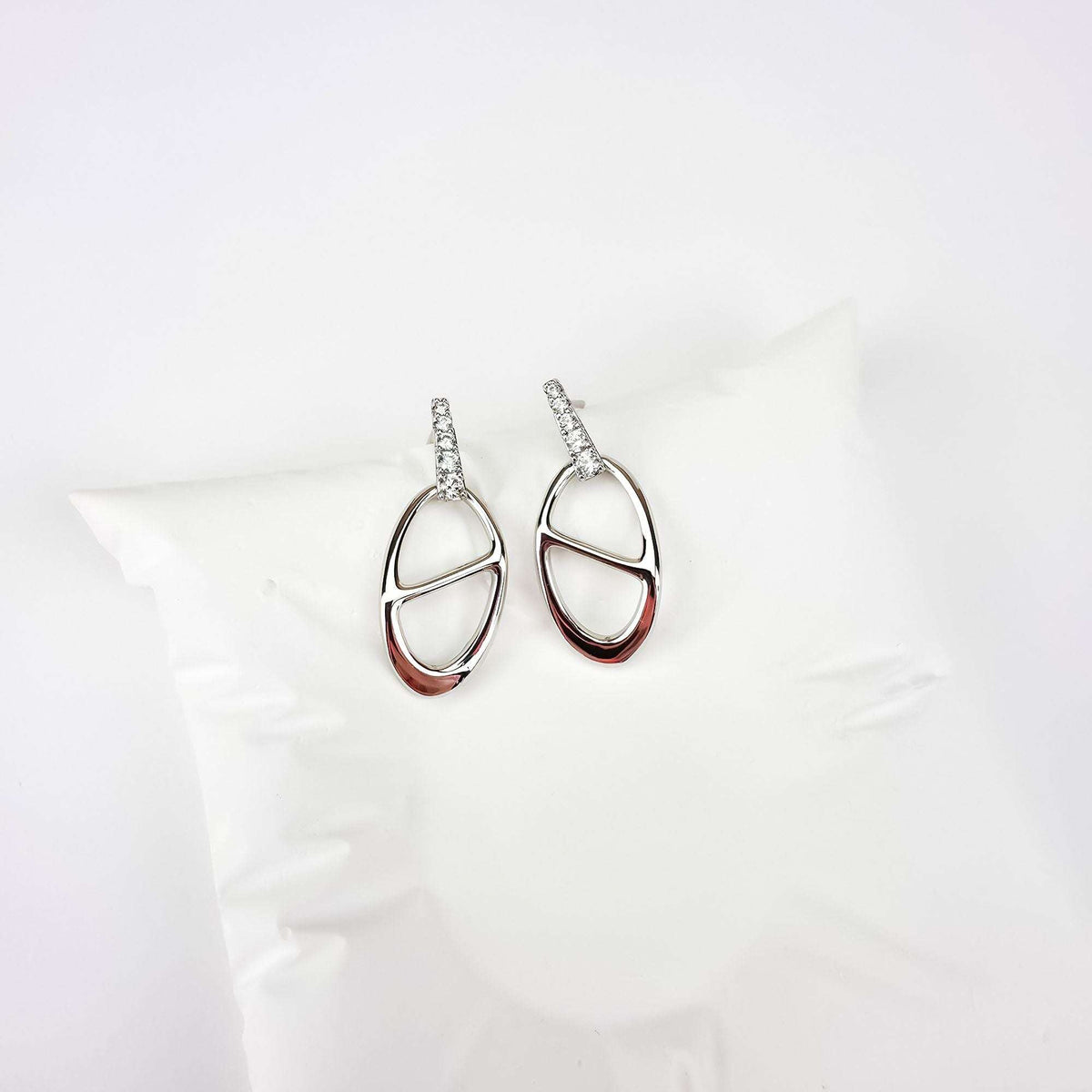 Mirror-bright oval earrings with cubic zirconia on a white fabric cushion