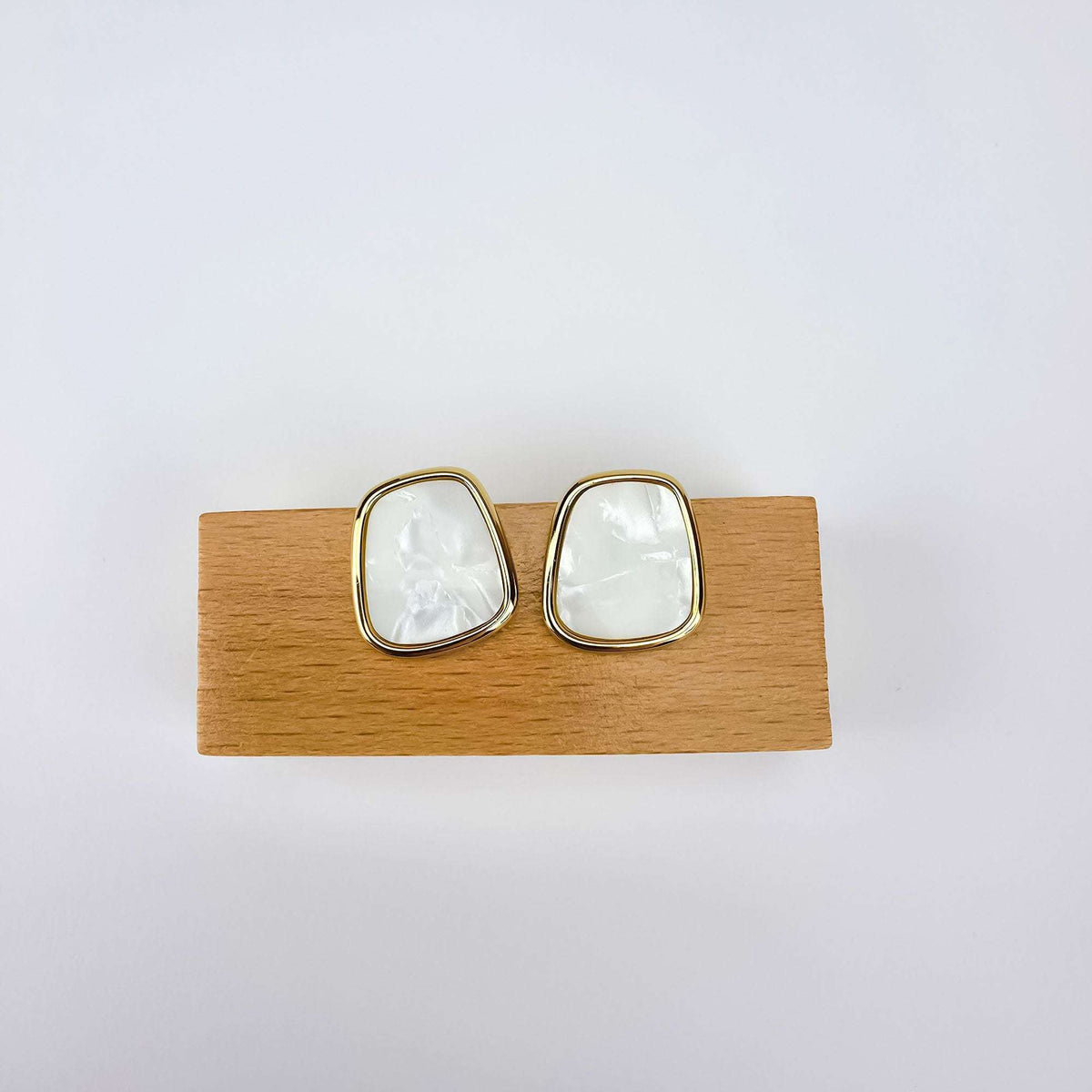 Pair of pearly white earrings on a wooden stand, smooth gold-tone frame