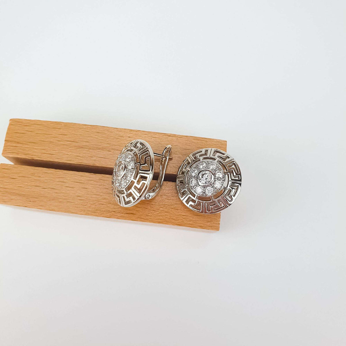 Pair of round Greek pattern earrings on a wooden stand