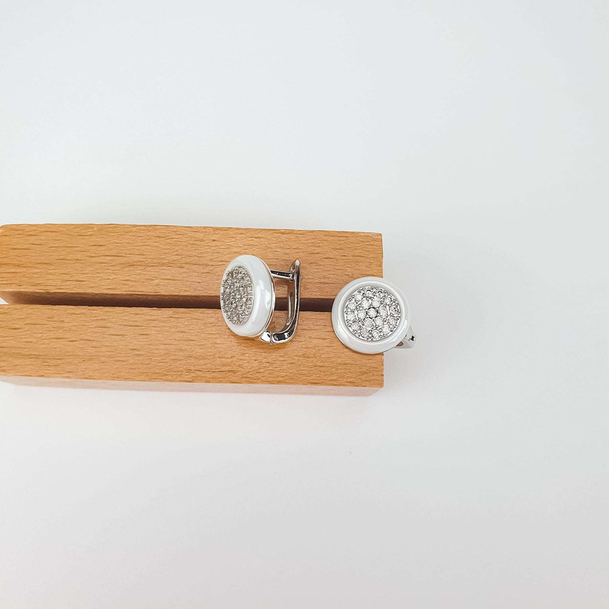 Pair of round white ceramic earrings with cubic zirconia on a wooden stand