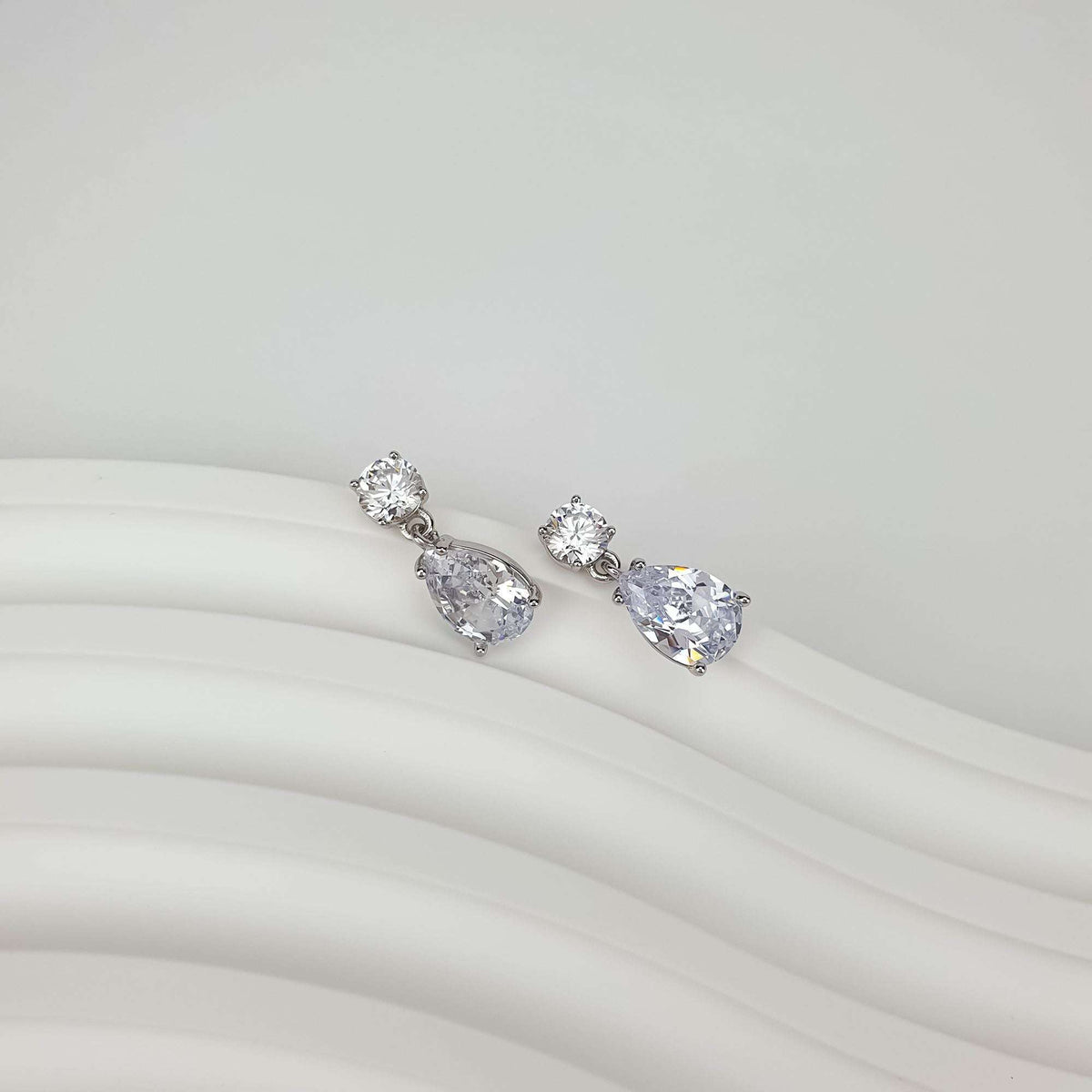 Teardrop cubic zirconia earrings lying diagonally on soft white fabric, facets visible