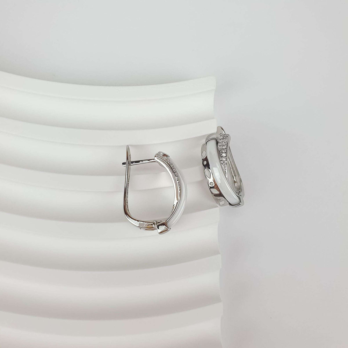 Side view of rhodium-plated earrings with glossy white inlay and sparkling stones
