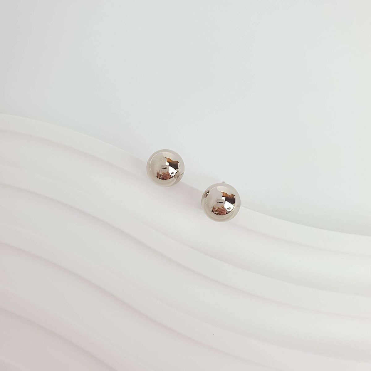 Minimalist studs with small shiny platinum-tone balls on a wavy background