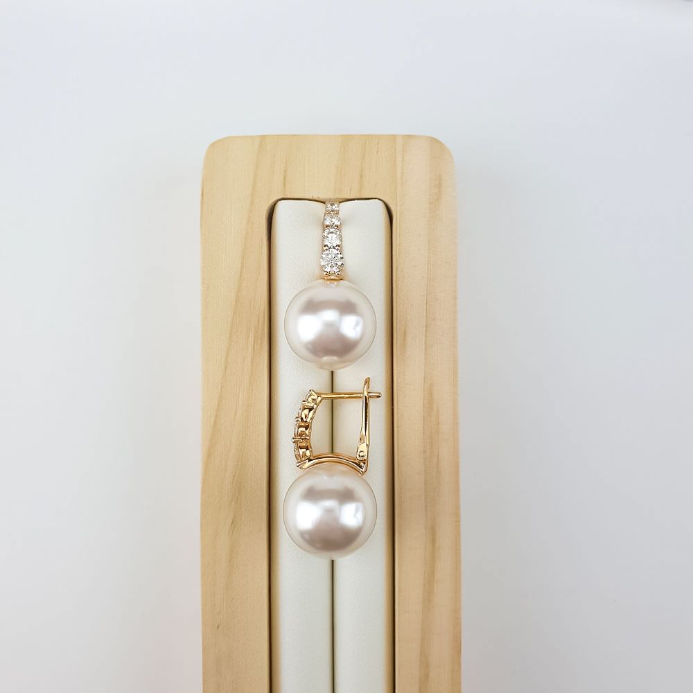 Pair of faux pearl earrings on a light wooden stand, gold-plated clasp detail visible