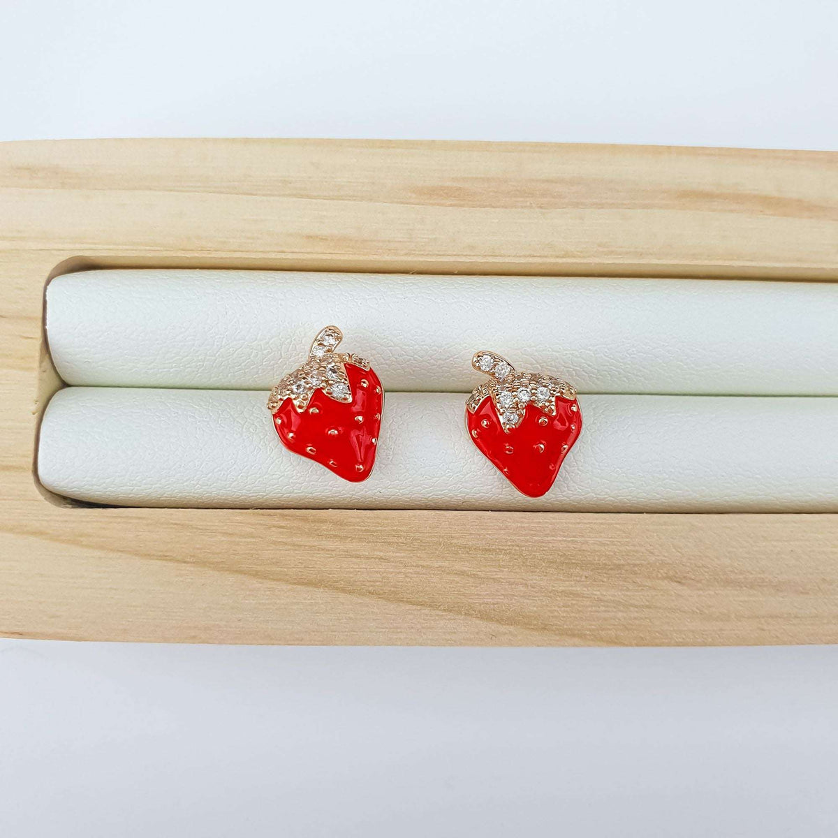 Red enamel strawberry earrings on a wooden stand with a light leather insert