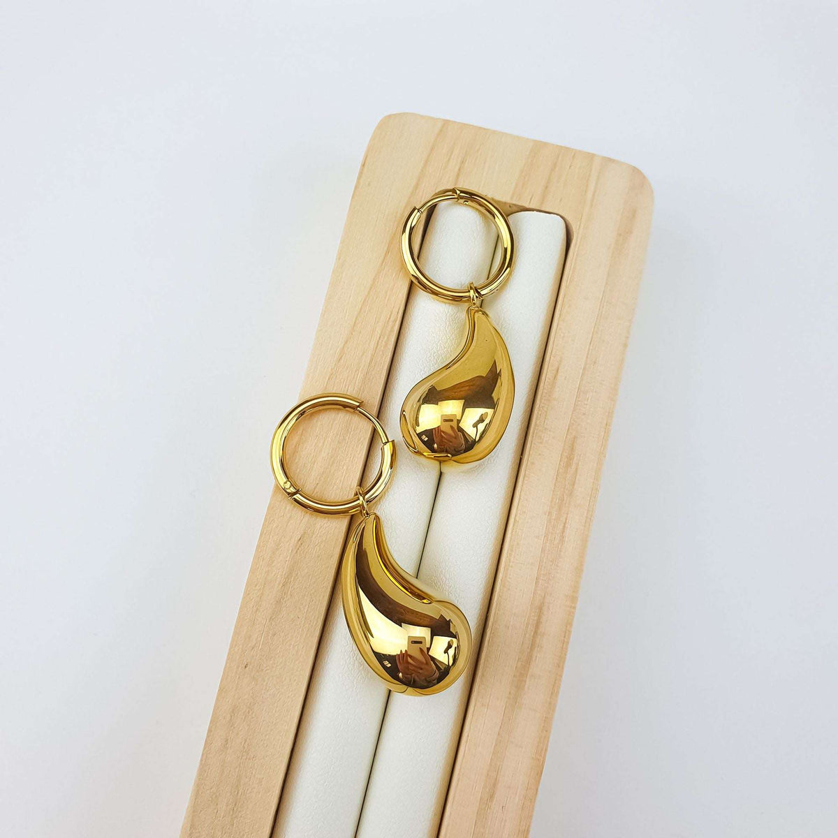Gold-plated hoop earrings with a large smooth teardrop on a wooden stand