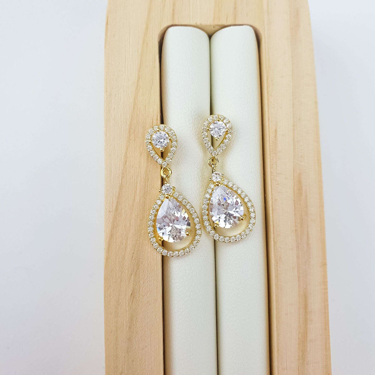 Teardrop cubic zirconia earrings with gold plating on a wooden stand