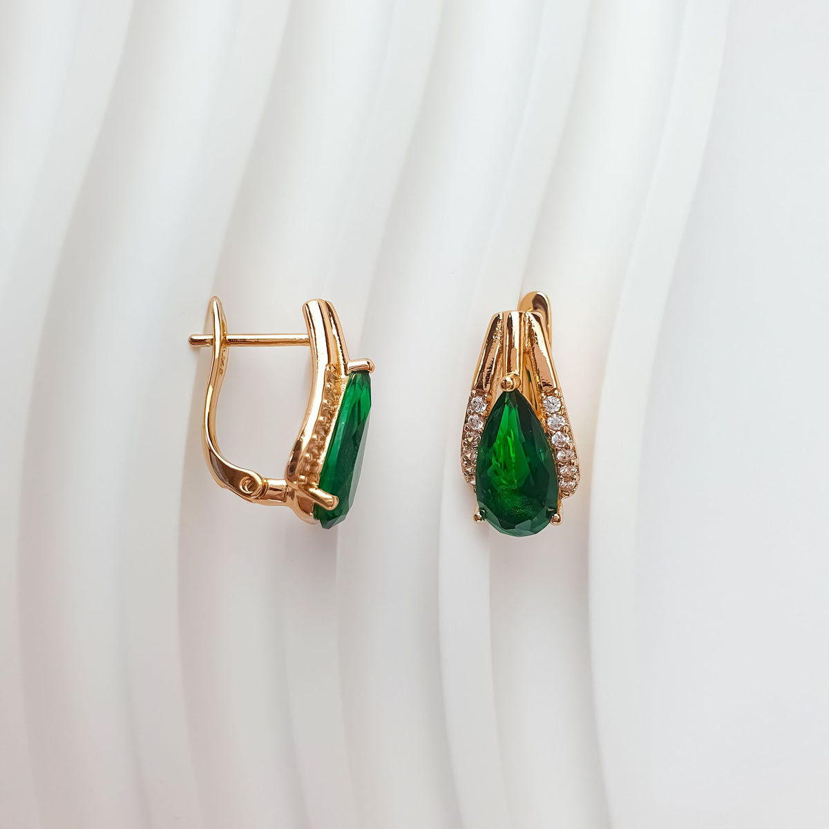 Green teardrop earrings on white fabric, side view of the clasp