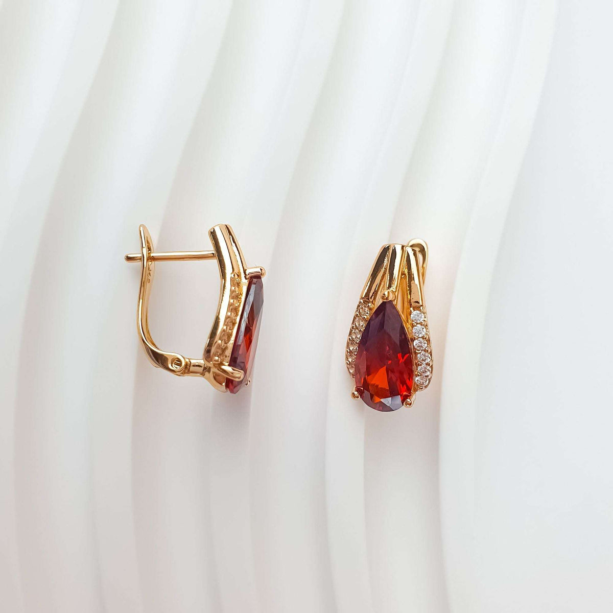 Two red cubic zirconia earrings on white fabric, leverback clasp from the side