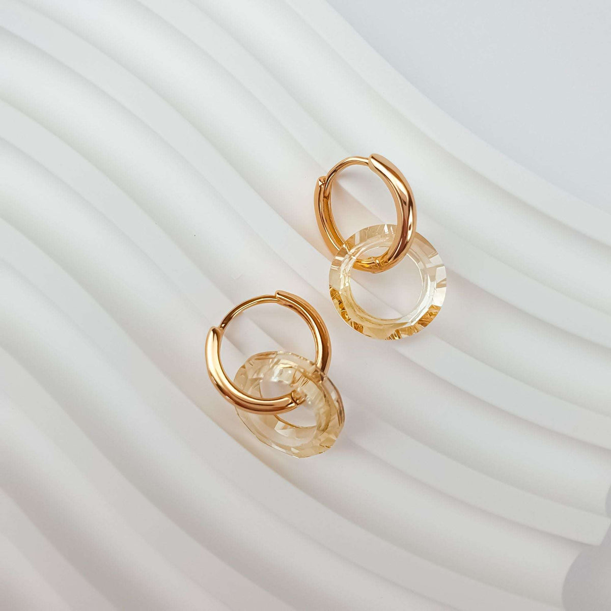 Pair of gold-plated round earrings with champagne crystal rings on white fabric