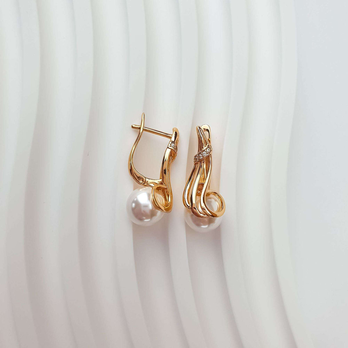 Pair of gold-plated pearl earrings on a wavy background showing the leverback clasp