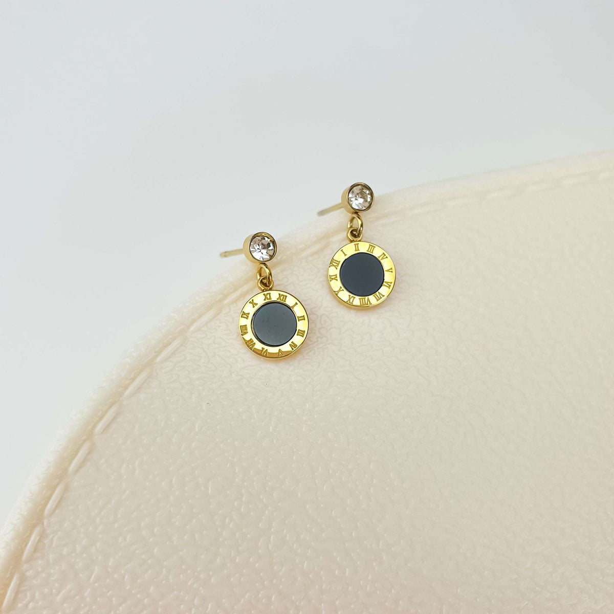 Pair of gold-plated earrings close up on a cream surface, stud posts visible
