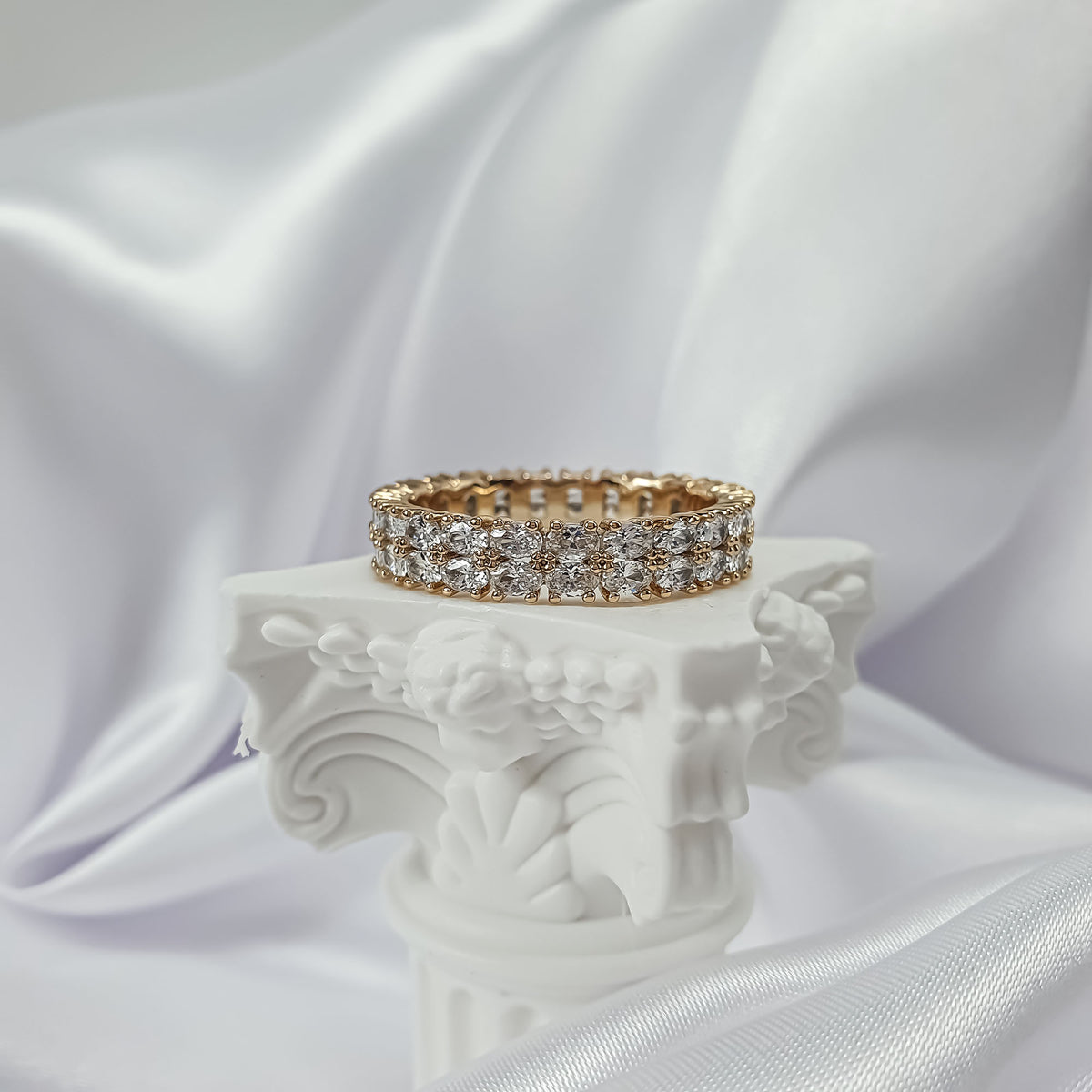 Gold-plated eternity ring with clear crystals on a white antique pedestal