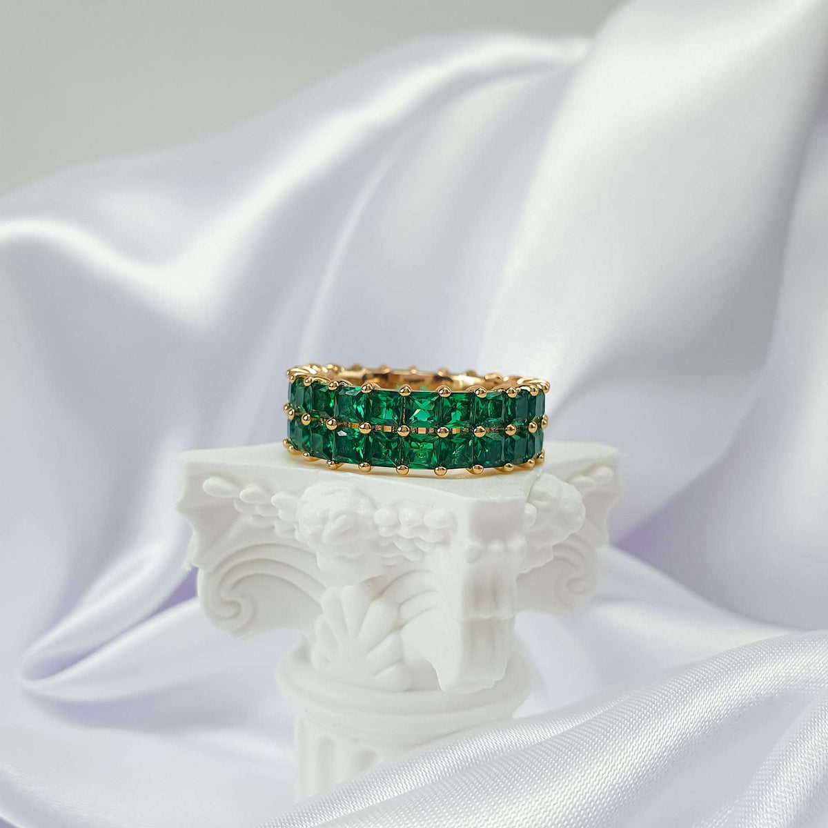 Green crystal ring with gold plating on a white column pedestal